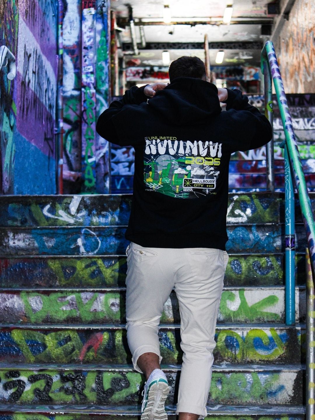 Back of the black hoodie, green and white Neon State of Mind print, on a graffiti-covered staircase.