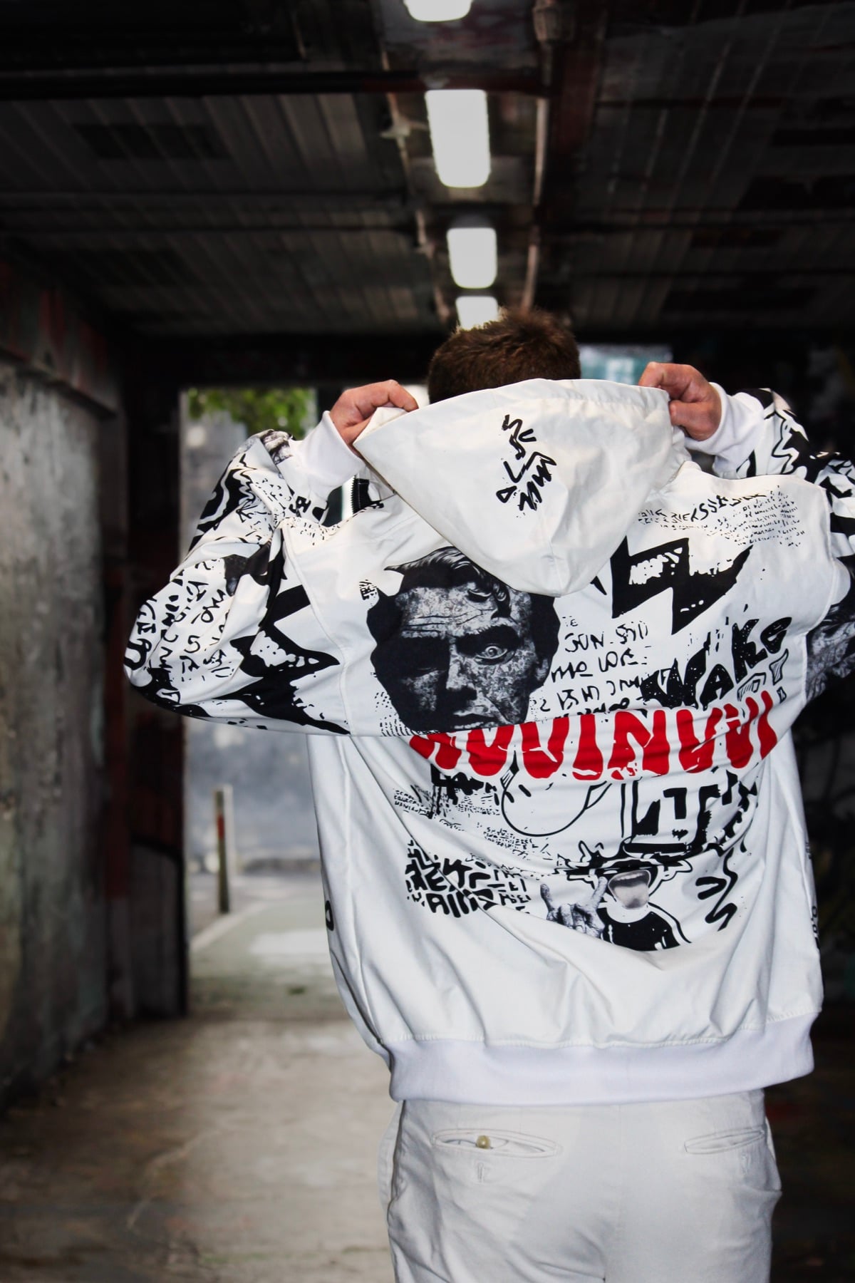 Back of the VINV white graffiti jacket, hood held in both hands, red NVVINVVI print