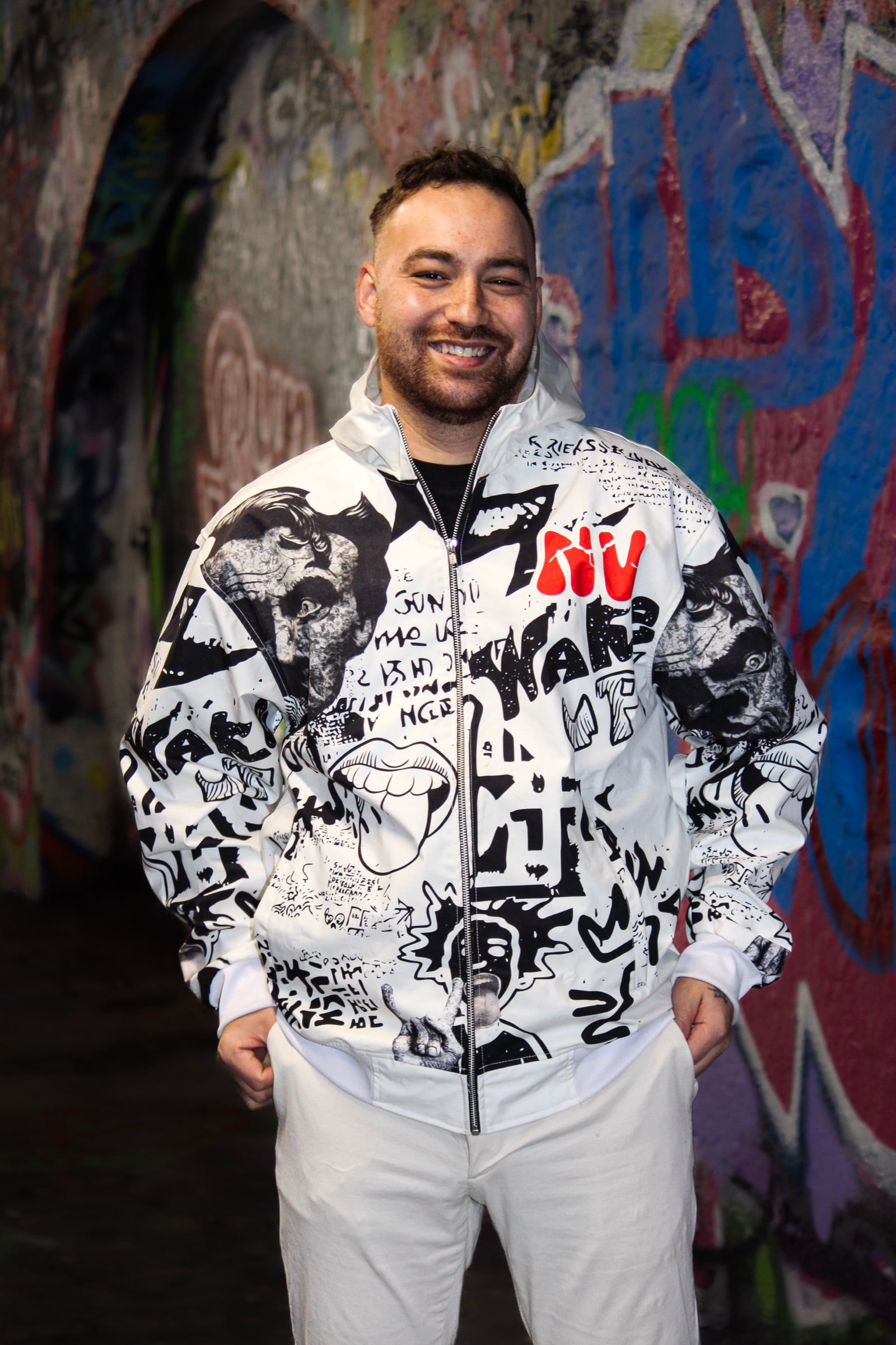 VINV white graffiti jacket worn from the front, zipped up, in front of a colourful graffiti wall