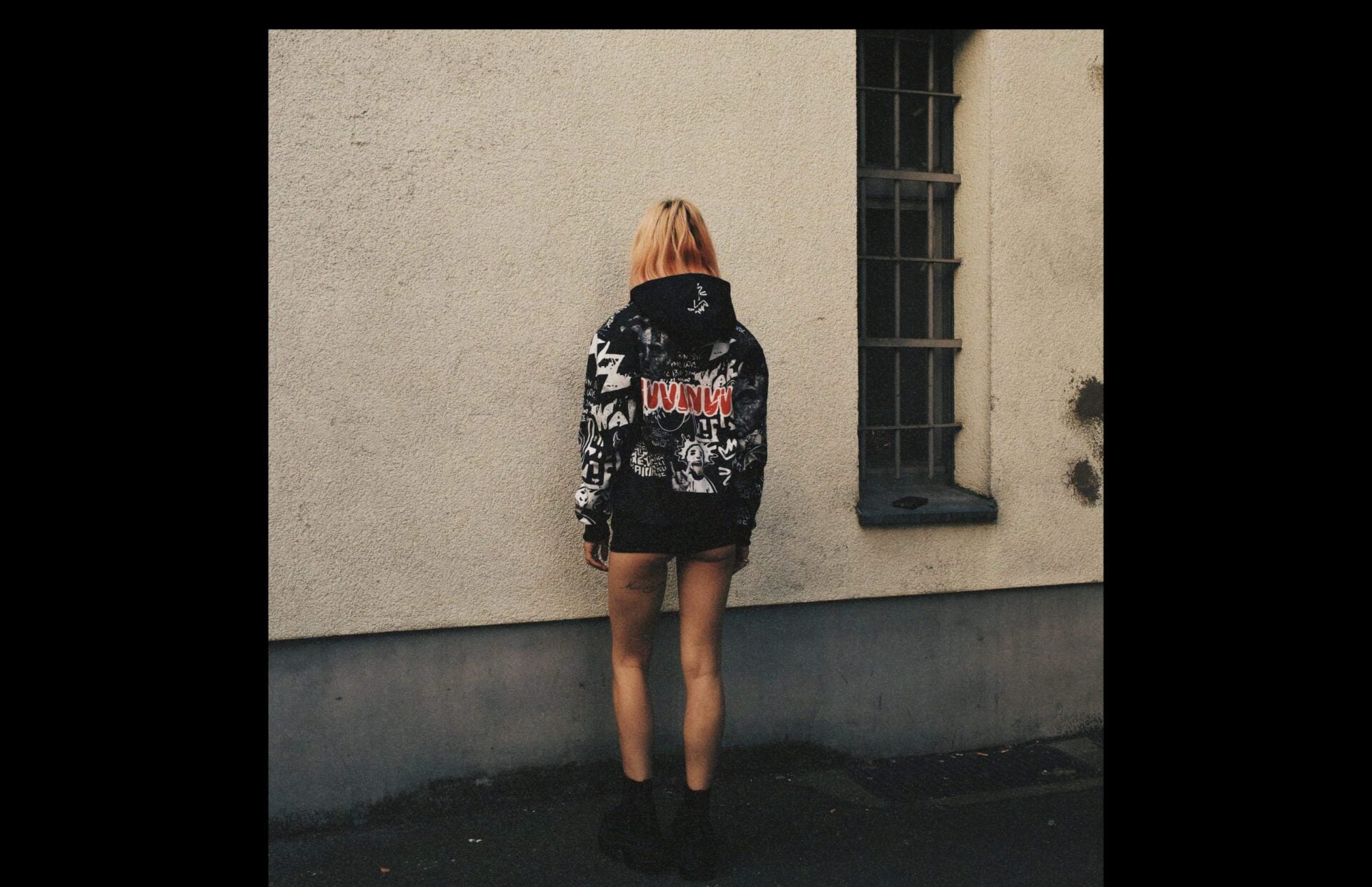 Veste graffiti noir et blanc portée de dos, debout contre un mur clair.