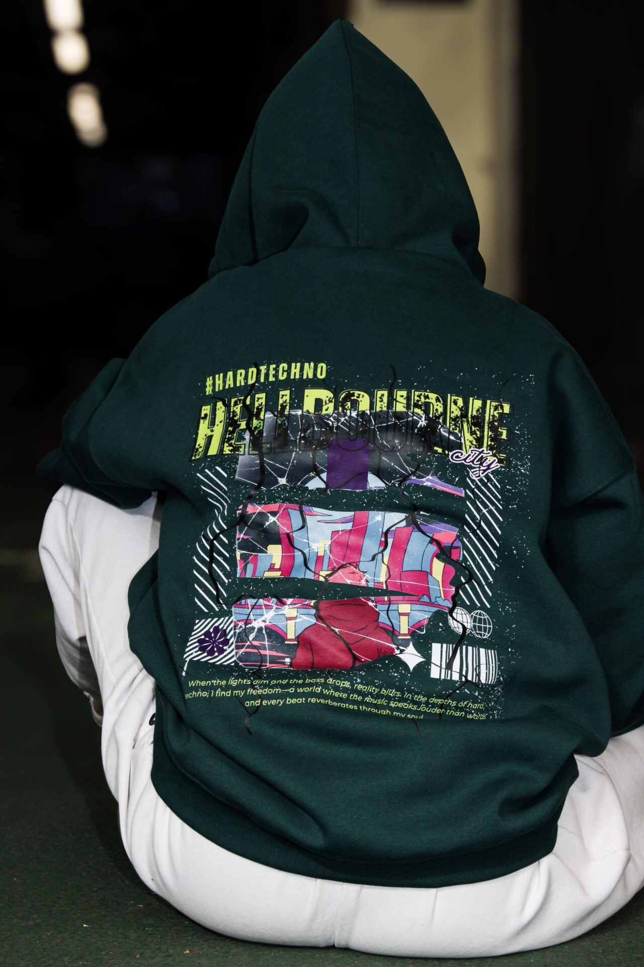 Dos du hoodie vert, grande impression dorsale illustrée, assise au sol.