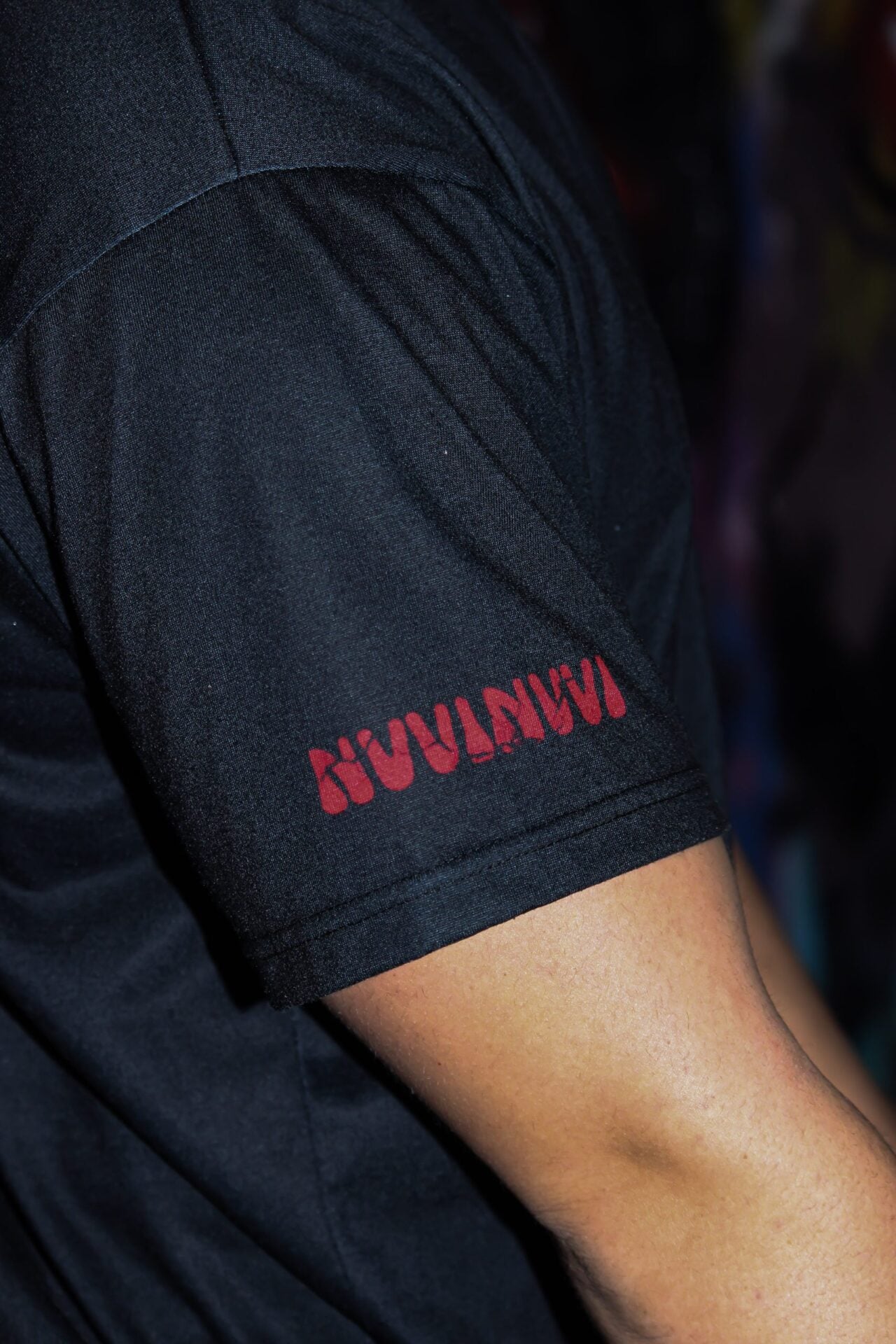 Détail de la manche du t-shirt noir, lettrage NVVINVVI rouge.