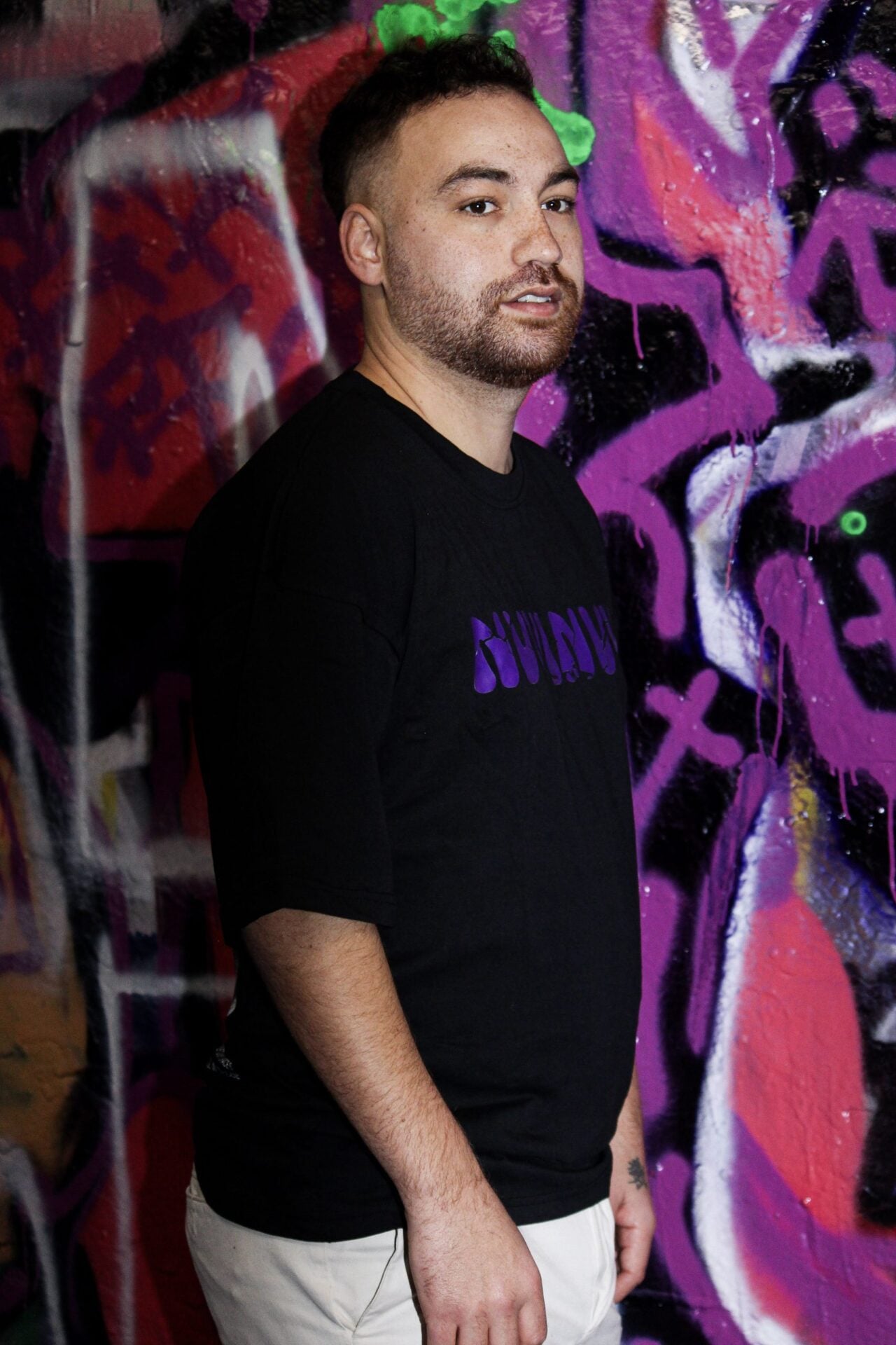 T-shirt noir porté de face, lettrage NVVINVVI violet sur la poitrine.