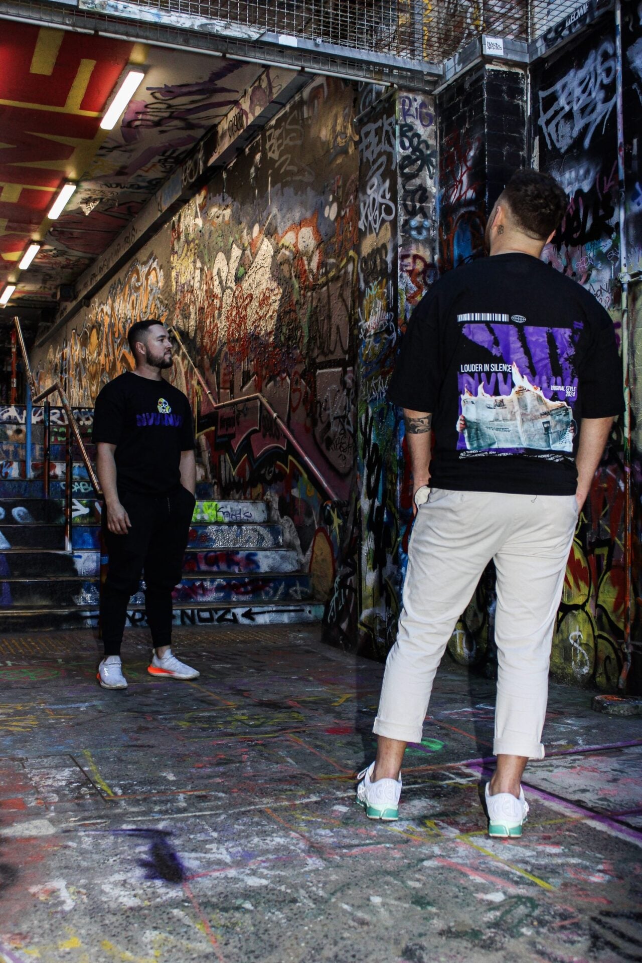 T-shirt noir porté de dos dans un tunnel couvert de graffitis, impression dorsale violette.